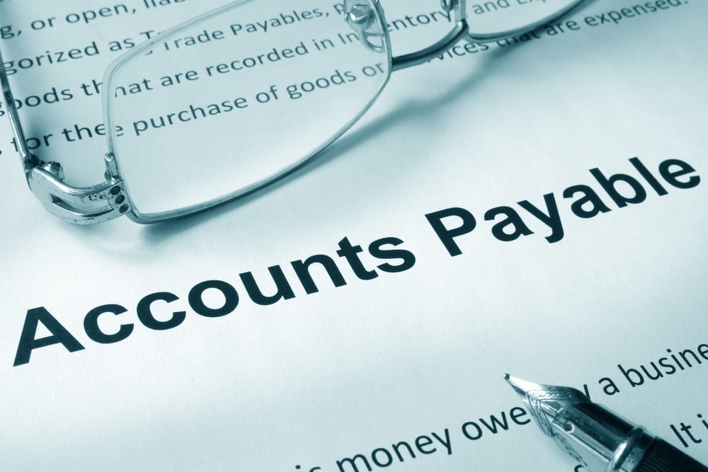 Close-up of a document titled "Accounts Payable" with reading glasses and a fountain pen resting on the page.