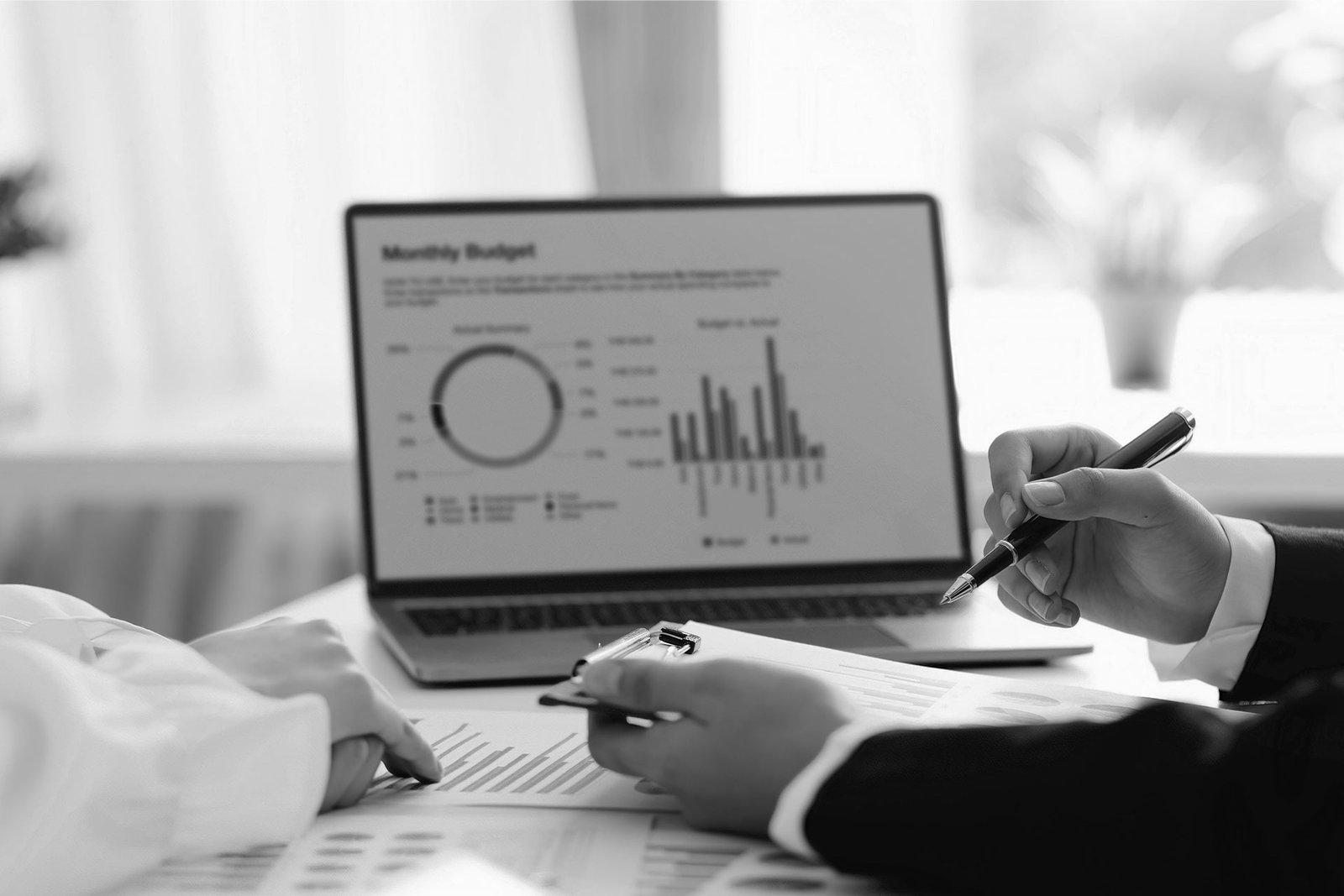 Financial planning meeting with professionals reviewing a monthly budget report, analyzing charts and business performance data on a laptop.